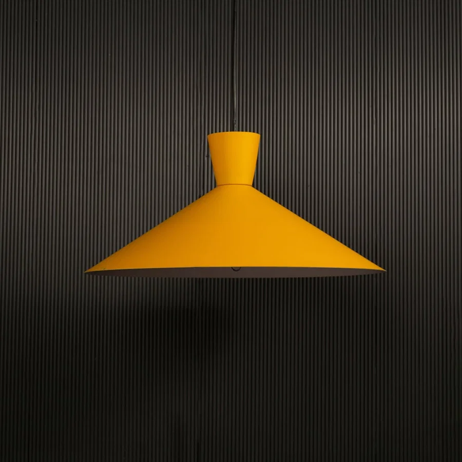 Yellow cone pendant light hanging against dark textured wall with light on for bright modern décor.