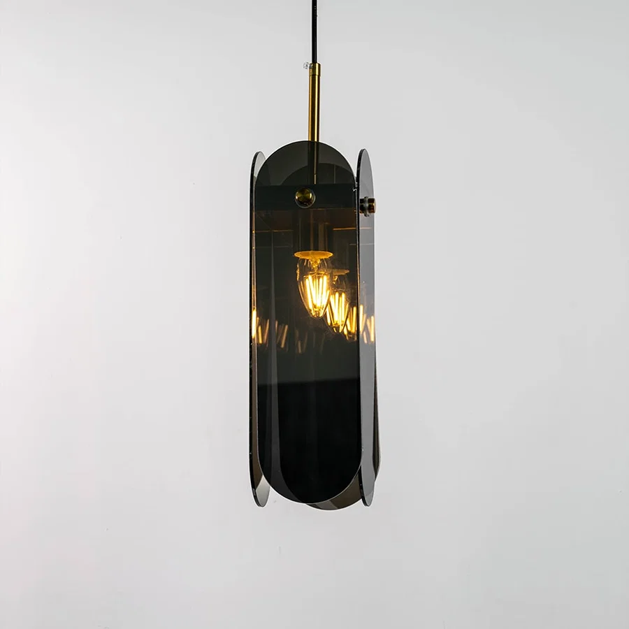 Grey glass pendant light displayed with light on against a dark background enhancing its warm illumination reflective finish and gold detailing.