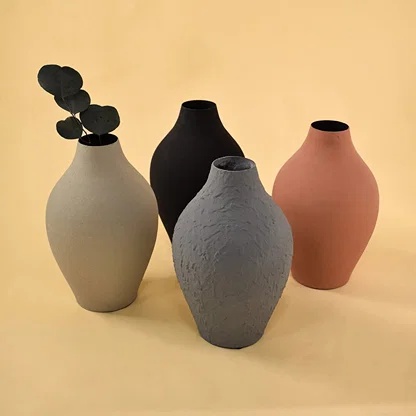 A curated arrangement of four vases in black grey terracotta and cream tones displaying varied textures and shapes for a stylish modern decor composition.