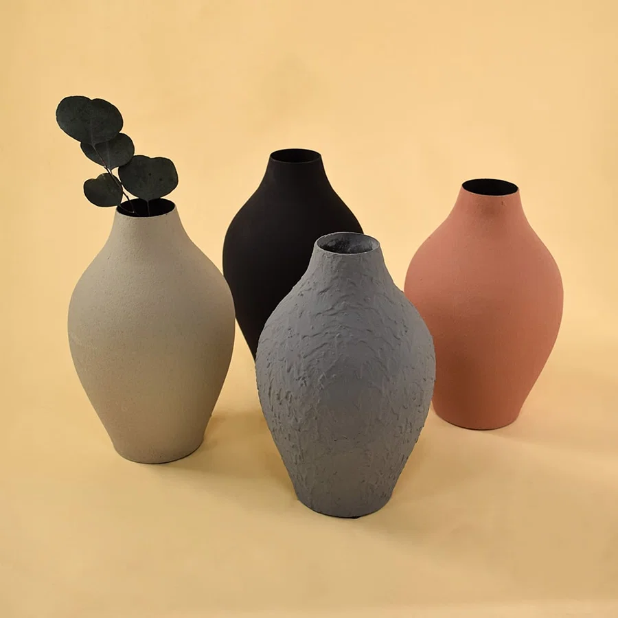 A curated arrangement of four vases in black grey terracotta and cream tones displaying varied textures and shapes for a stylish modern decor composition.