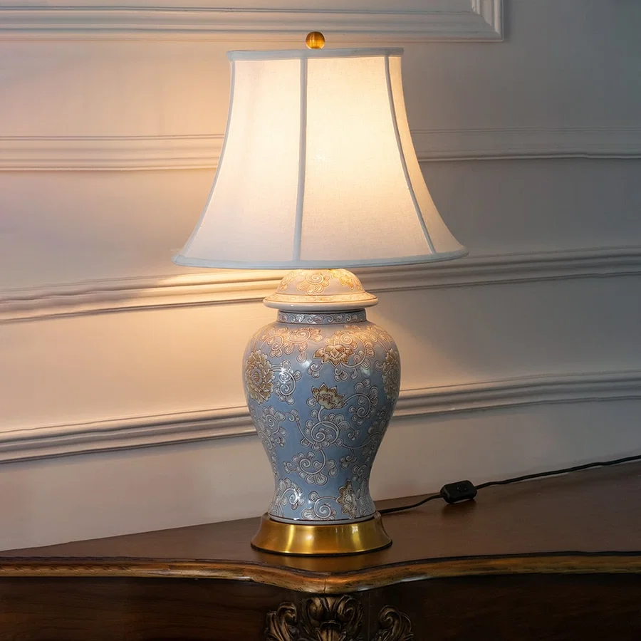 Blue ceramic table lamp with fabric shade displayed on a wooden console table creating warm traditional ambient lighting.