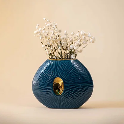Blue oval ceramic vase with gold accent featuring ribbed texture and glossy finish displayed on beige background.