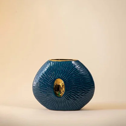 Contemporary blue oval ceramic vase with ribbed design and gold detailing displayed on plain White background.