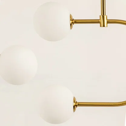 Gold metal pendant light closeup showcasing smooth white glass globes and refined modern decorative detailing.
