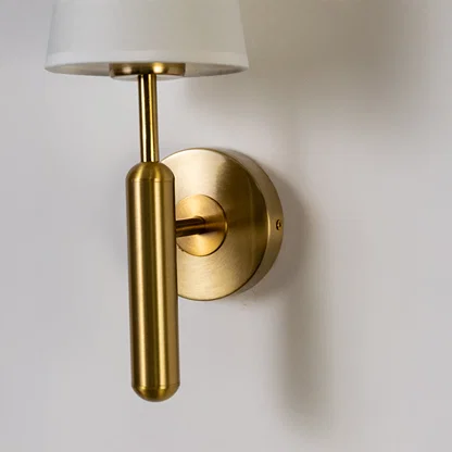 Modern wall light in gold metal finish with cylindrical arm for bedroom or living decor lighting placement white background.