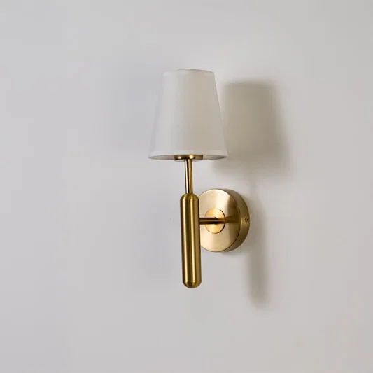 Gold metal wall light with white fabric shade displayed on a white background with light off highlighting its sleek minimal contemporary form.