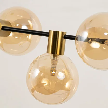Close view of amber glass chandelier showing sleek black rod polished gold fittings and smooth glass globes for modern decor.