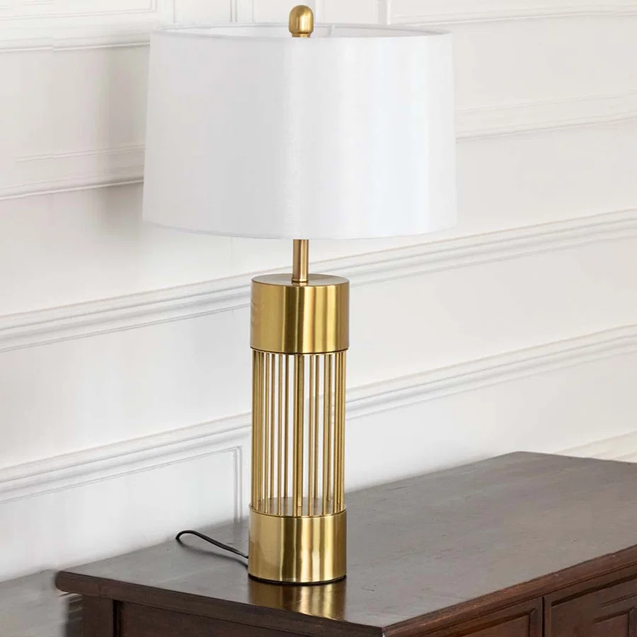 Tall gold lamp with clear glass accents on wooden table with light off and white wall background for luxury minimalist décor.