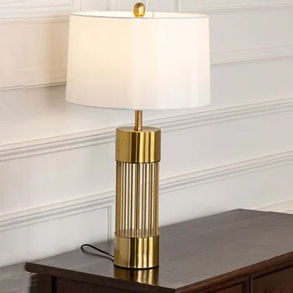 Gold metal table lamp with white fabric shade and open frame base creating elegant modern ambient lighting indoors.