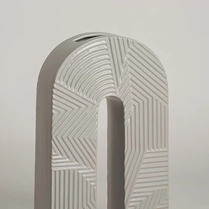 Closeup image of a modern arch shaped grey ceramic vase featuring intricate geometric relief linear stripe patterns.
