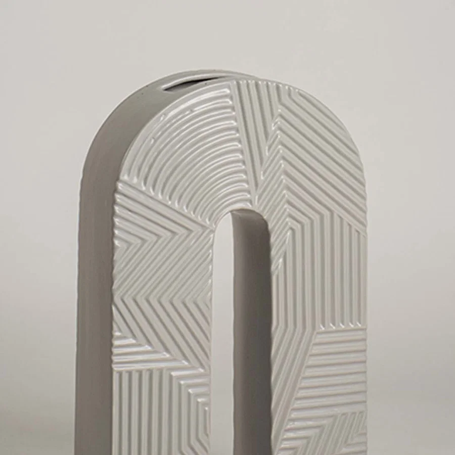 Closeup image of a modern arch shaped grey ceramic vase featuring intricate geometric relief linear stripe patterns.