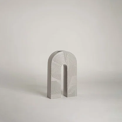 Modern arch shaped grey ceramic vase with geometric linear relief patterns on white background for minimalist art decor.