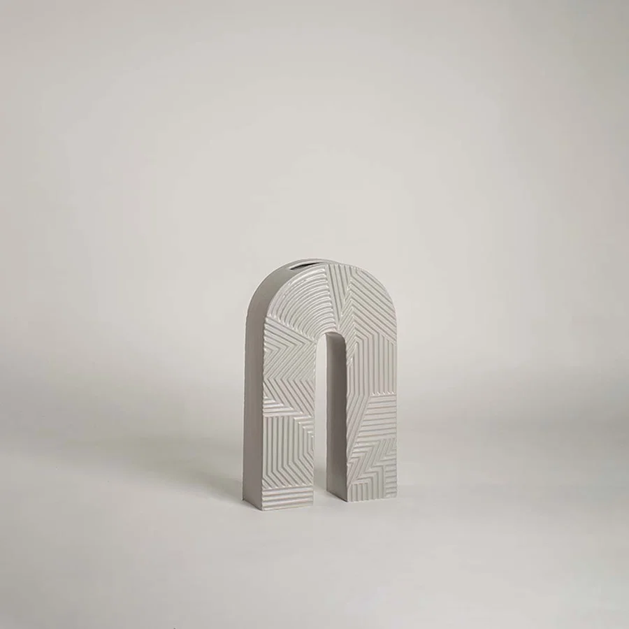 Modern arch shaped grey ceramic vase with geometric linear relief patterns on white background for minimalist art decor.