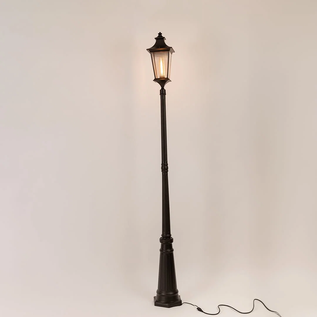 Black metal outdoor lamp post with illuminated clear glass lantern shown on white background for exterior decor display.