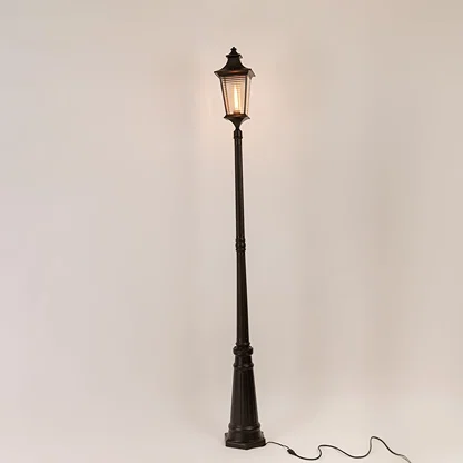 Black metal outdoor lamp post with illuminated clear glass lantern shown on white background for exterior decor display.