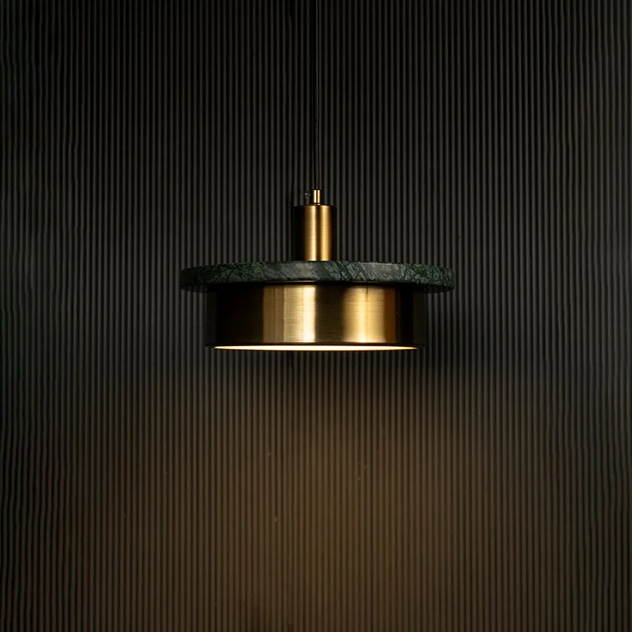 Green marble and metal disc pendant light hanging against dark textured wall with light on for stylish modern décor.