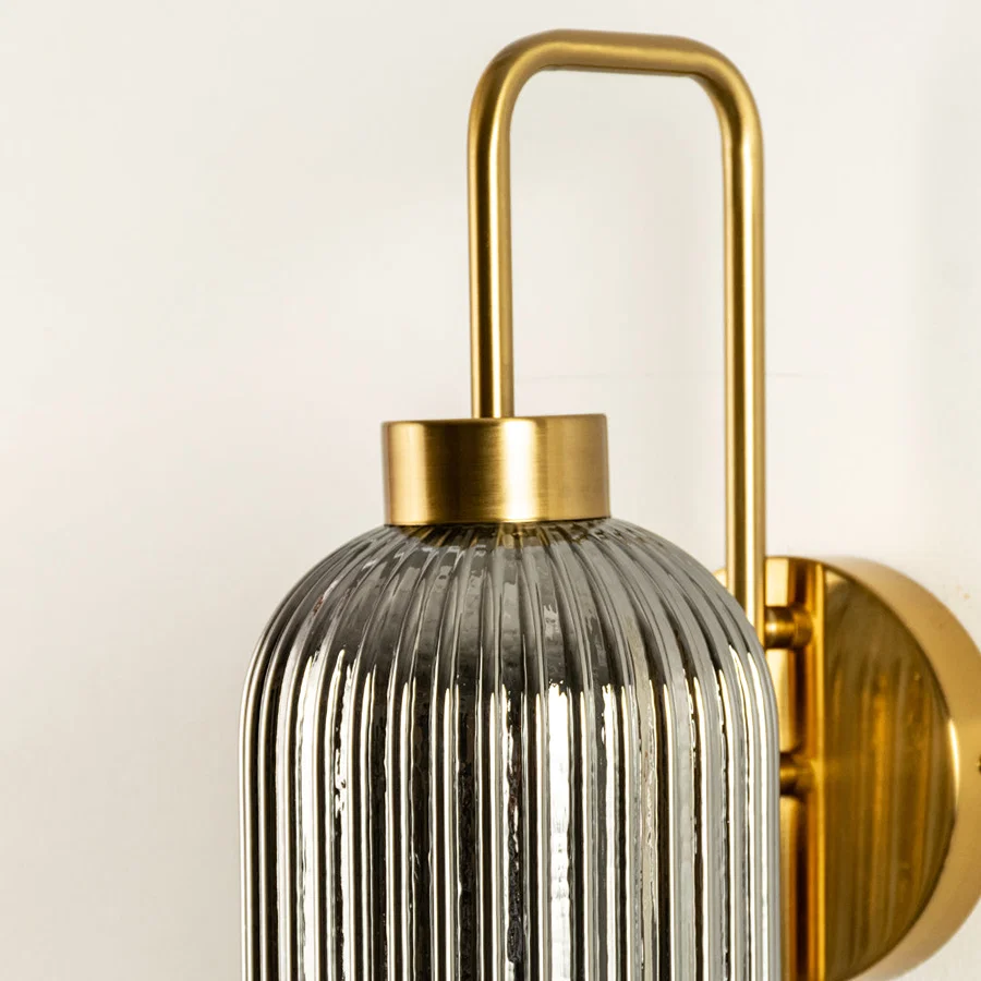 Closeup of gold metal wall light with ribbed glass shade showcasing detailed texture and premium finish for interior decor styling.