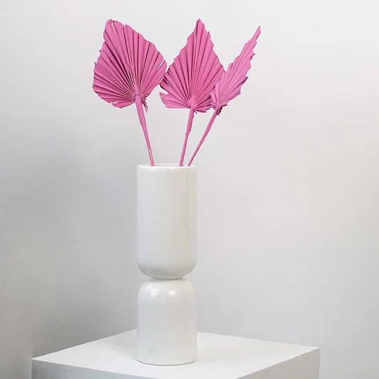 Pink dried palm leaves in tall white vase styled for modern home decor and boho table decoration.