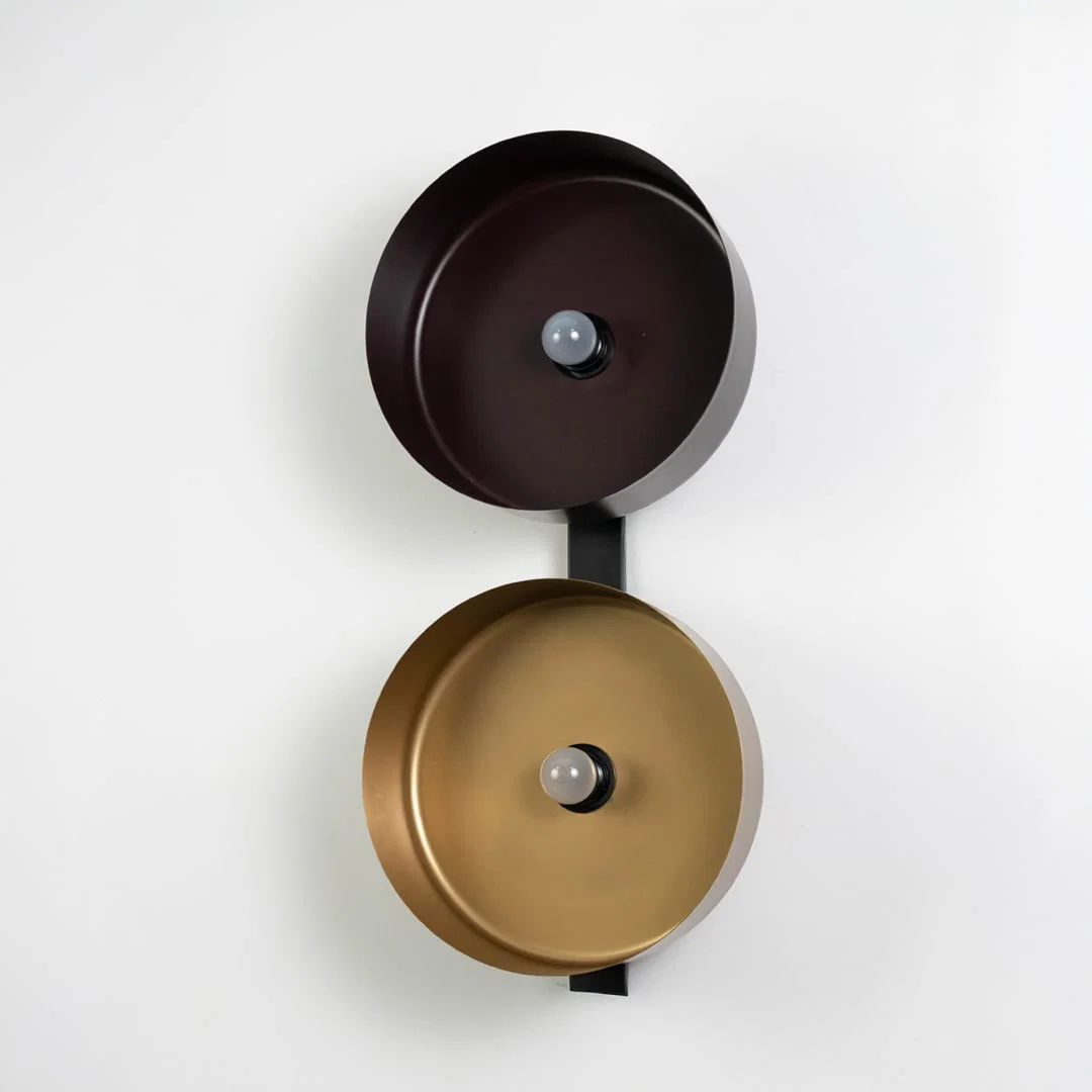 Bronze and gold reflector wall light mounted vertically on matte black base against clean white backdrop.