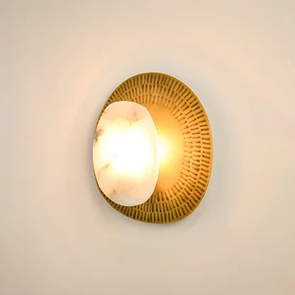Contemporary alabaster wall sconce illuminated on white background with textured brass plate offering a soft  warm glow and sophisticated appeal.