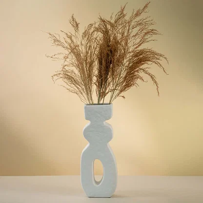 White sculptural ceramic vase with tall modern silhouette and hollow center styled with dried pampas grass.