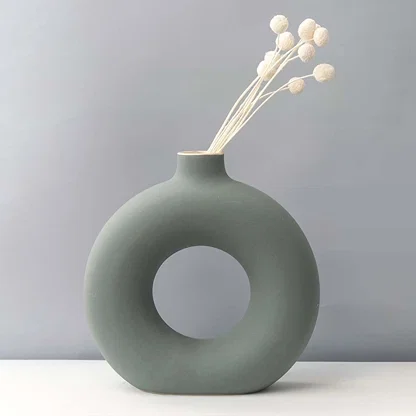 Grey round ceramic vase with hole design styled with white dried flower stems modern home decor accent for table.
