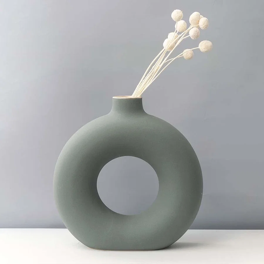 Grey round ceramic vase with hole design styled with white dried flower stems modern home decor accent for table.