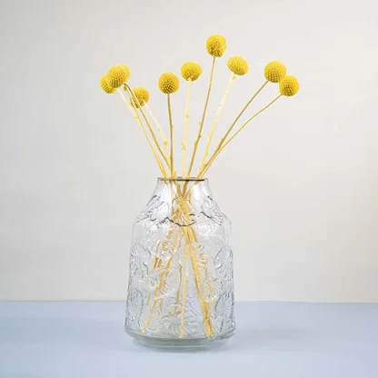 Clear glass vase with embossed design styled with yellow dried flower stems modern home decor accent for table.