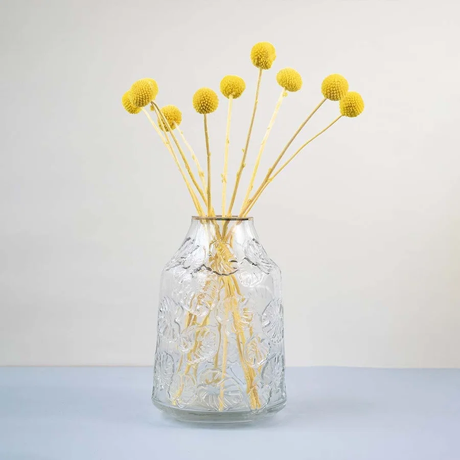 Clear glass vase with embossed design styled with yellow dried flower stems modern home decor accent for table.