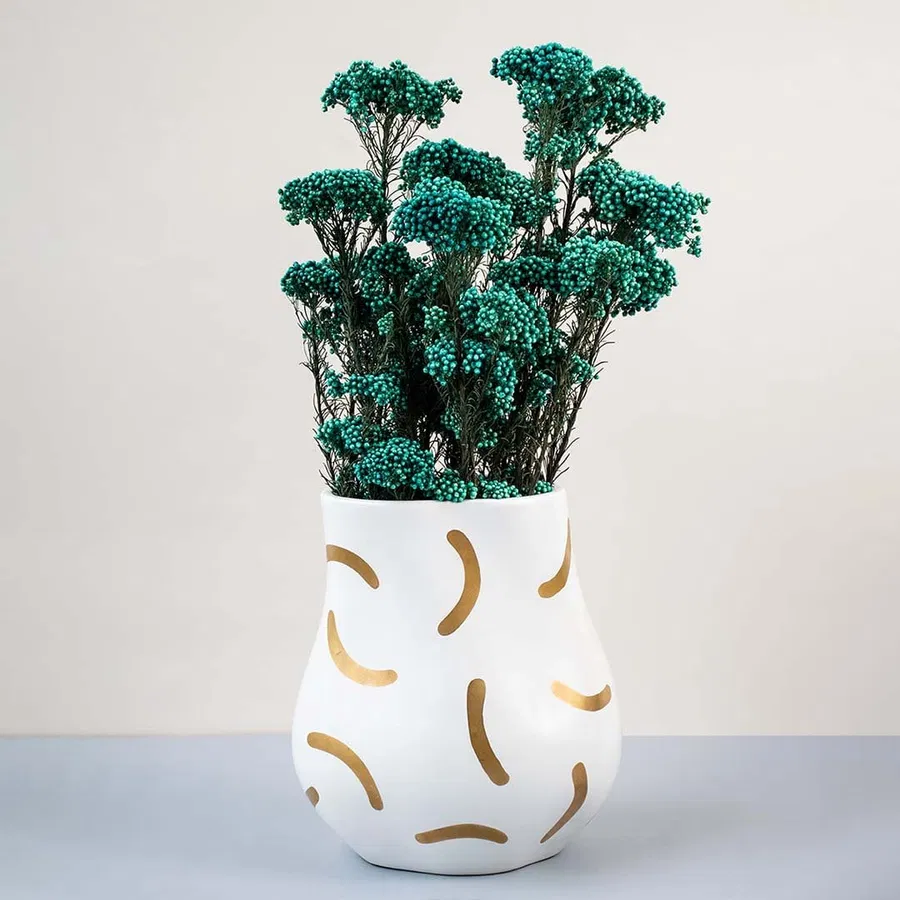 Green dried statice flower stems arranged in modern white ceramic vase with gold patterns elegant lifestyle decor.