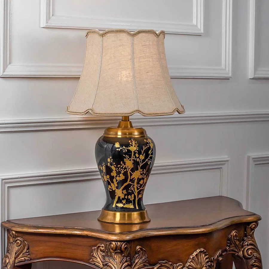 Black and gold floral table lamp with beige shade on carved console table with light on and white panel wall background for classic luxury d‚àö¬¢¬¨√†¬¨√∂‚àö√á¬¨¬©cor.