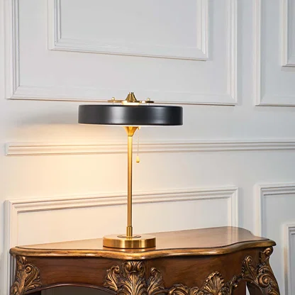 Black and gold metal table lamp with circular shade styled on a wooden console table offering contemporary decor lighting.