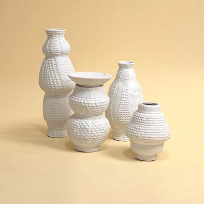 Set of artistic white ceramic vases with sculpted textures arranged together on white background creating a stylish modern decor look.