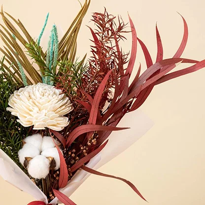 Closeup of dried bouquet with shola flower cotton stem palm leaf and red eucalyptus wrapped in white paper with satin ribbon.