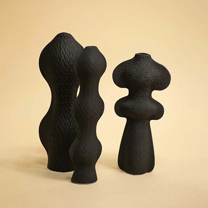 Set of black sculptural vases with unique artistic shapes arranged together on a soft white background for a modern decor look.