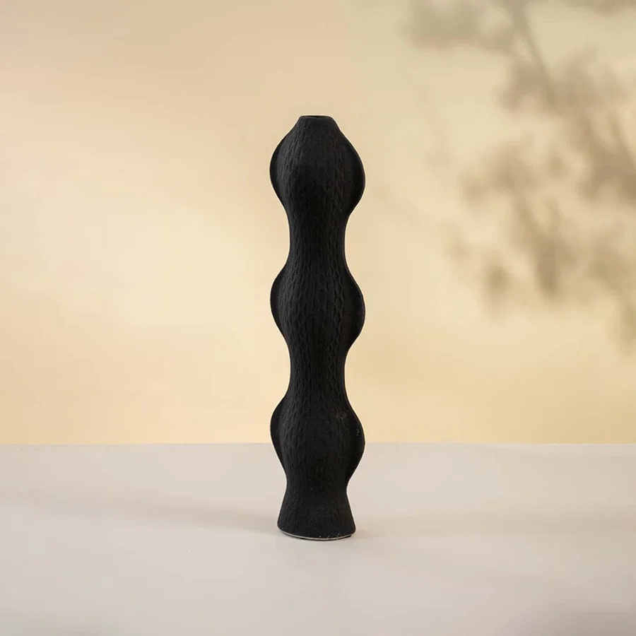 Contemporary black vase softly lit against a white backdrop highlighting its artistic shape and surface texture.