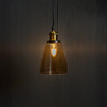 Gold glass pendant light with brass and black holder turned on glowing warmly against plain black background.