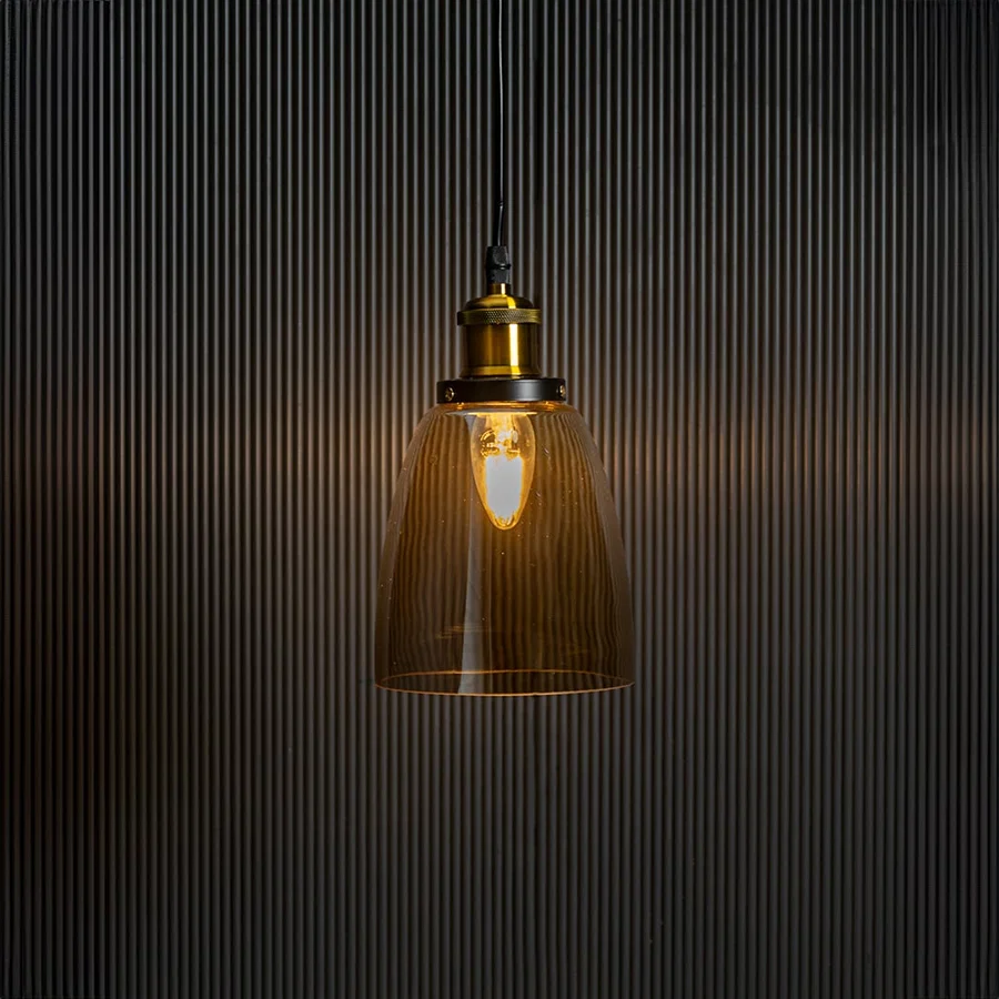 Gold glass pendant light with brass and black holder turned on glowing warmly against plain black background.