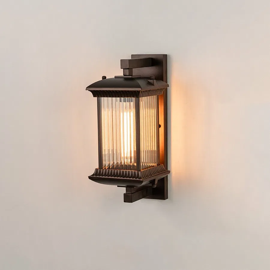 Antique bronze metal outdoor wall light on white background with ribbed glass shade illuminating warm patio decor.