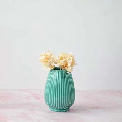 Stylish ribbed vase in green placed on pink marble surface beautifully enhancing home interior style.