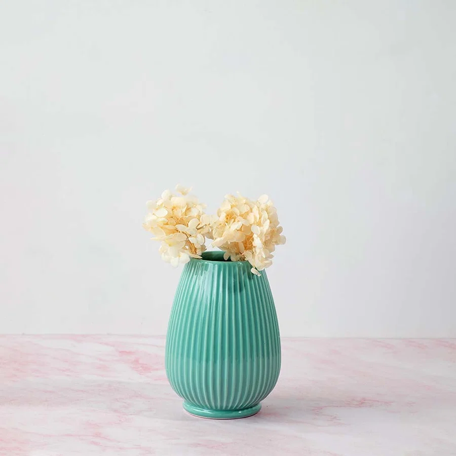 Stylish ribbed vase in green placed on pink marble surface beautifully enhancing home interior style.