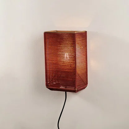 Modern rectangular rust red twine wall lamp turned on against a plain off white background to show the cozy light pattern.