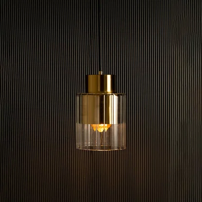 Gold metal and glass pendant illuminated against a dark backdrop highlighting its soft light and reflective metallic surface.
