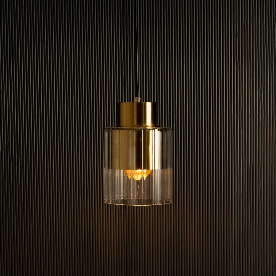 Gold metal and glass pendant illuminated against a dark backdrop highlighting its soft light and reflective metallic surface.
