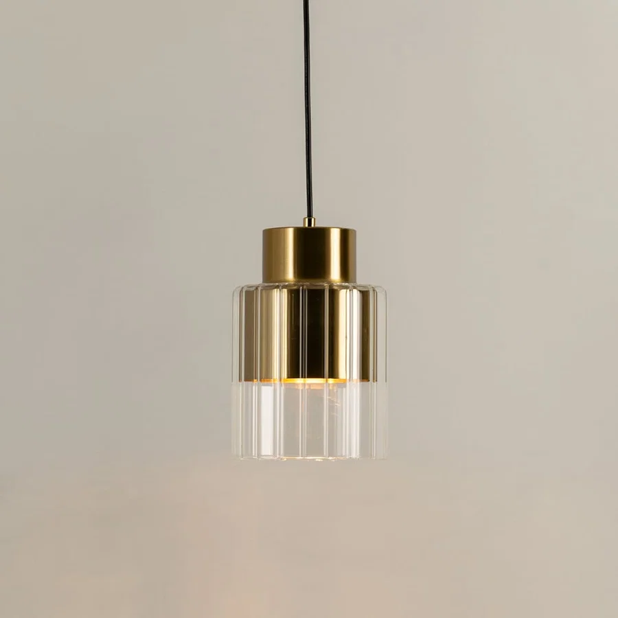 Gold metal pendant light with clear glass diffuser illuminated to highlight premium modern decorative lighting.