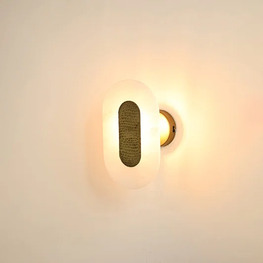Oval alabaster wall sconce illuminated on white background featuring warm brass texture and soft diffused glow ideal for luxury home lighting.