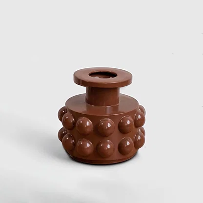 A modern brown sculptural vase with bold raised circular details displayed on a clean white background showing its artistic contemporary form.