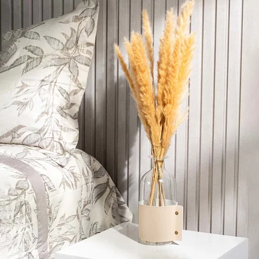 Elegant dried pampas grass in clear glass vase with beige leather strap styled on bedside table for home decor.