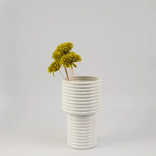 Olive green handmade sola wood flower stems arranged inside a modern white ribbed ceramic vase for bedroom tabletop decor.