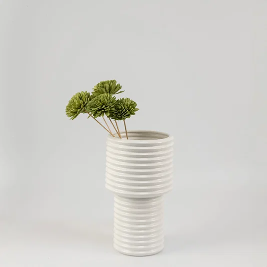 Moss green handmade sola wood flower stems arranged inside a modern white ribbed ceramic vase for bedroom tabletop decor.
